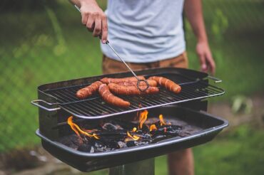 bbq with 6 frankfurter sausages and a man stood turning them over