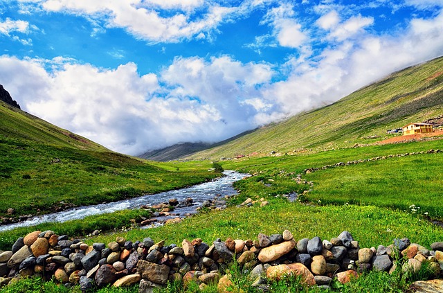 beautiful scenery of a stream running between two grassy hills and a beautiful blue sky ditted with white clouds. Nature and the great outdoors at its best.