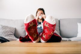 Blurry image of a woman sat on a sifa with her feet up on the table drinkng a cup of teea. her feet are at the front of the photo and they are covered with red reindeer socks.