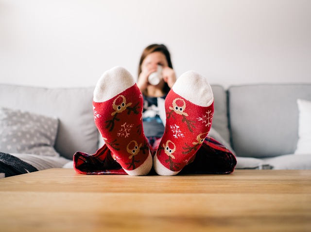 Blurry image of a woman sat on a sifa with her feet up on the table drinkng a cup of teea. her feet are at the front of the photo and they are covered with red reindeer socks.