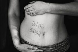black and white photo of a close up of a woman's stomach area with the words 'out of order' written in pen on the left hand side. Indcating she suffers from digestion problems.