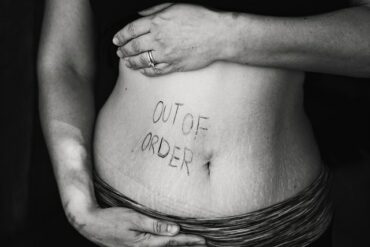 black and white photo of a close up of a woman's stomach area with the words 'out of order' written in pen on the left hand side. Indcating she suffers from digestion problems.