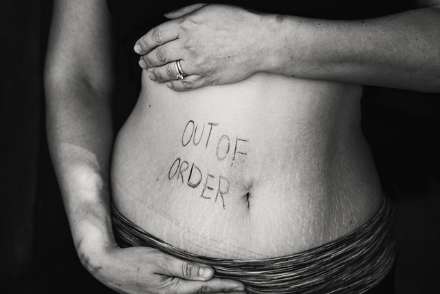black and white photo of a close up of a woman's stomach area with the words 'out of order' written in pen on the left hand side. Indcating she suffers from digestion problems.