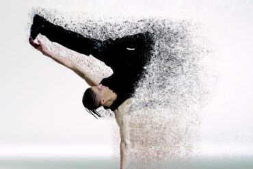 male dancer supporting himself on oone hand with the other one stretched out holding onto one of his legs. Half his body has faded away into little dts, making the image lok futuristic. Representing the future of fitness in the year 2020