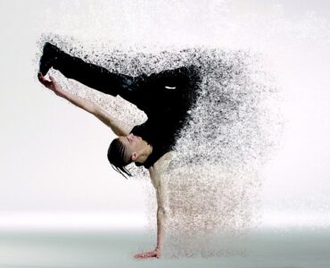 male dancer supporting himself on oone hand with the other one stretched out holding onto one of his legs. Half his body has faded away into little dts, making the image lok futuristic. Representing the future of fitness in the year 2020