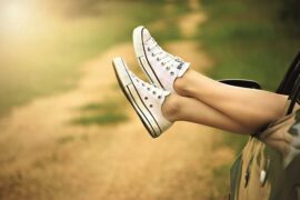pair of womens feet stickng out of a car window. She ss wearing canvas sneakers and the impression is that she is relaxed and loves life.