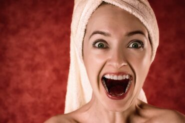 Female face and neck wth her mouth open showng healthy teeh. she has a towel wrapped around her head and looks really happy.