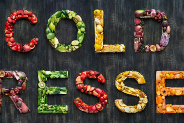 variety of fruts and vegetables laid out on a black background spelling out the words cold pressed