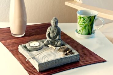 sm,all buddha statue sat in a square tray filled with sand. There is also a tealight candle, some stones and an incense stick. It indicates feng shui in the home