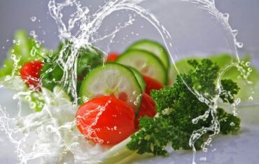 fresh foods ncluding sliced cucumber, tomatoes, lettuce and parsley with a jet iof fresh water leaping over it