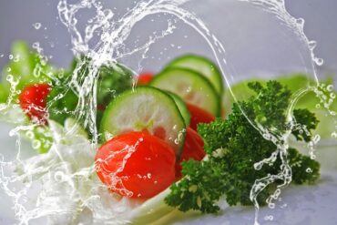 fresh foods ncluding sliced cucumber, tomatoes, lettuce and parsley with a jet iof fresh water leaping over it