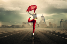 female wearing red troudrs and a stripy long sleveed top, jumping in the air while holding a rd scarf above her head. the background is a cityscape and it is meant to represent her lifestyle choices