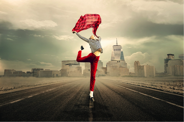 female wearing red troudrs and a stripy long sleveed top, jumping in the air while holding a rd scarf above her head. the background is a cityscape and it is meant to represent her lifestyle choices