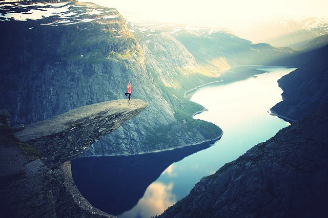 woman doing a yoga pose on the edge of a cliff overlooking a canyon with a river running through it. It represents the rise in popularity of novelty yoga