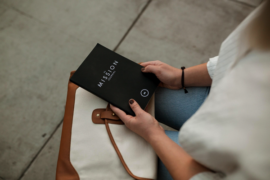 corner shot of a womans hands iin her lap holding a black book as she attempts to find purpose in life.
