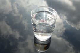 glass of water n a glass background that is reflecting a cloudy sky, suggesting water purification