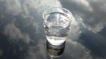glass of water n a glass background that is reflecting a cloudy sky, suggesting water purification