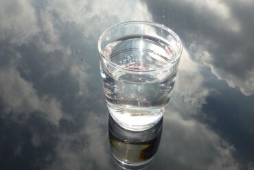 glass of water n a glass background that is reflecting a cloudy sky, suggesting water purification