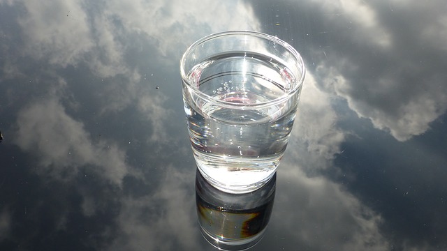 glass of water n a glass background that is reflecting a cloudy sky, suggesting water purification