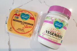 A pack of Follow Your Heart vegan cheese slices next to a jar of Follow Your Heart garlic aioli vegenaise on a white and grey veined marble background