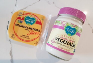 A pack of Follow Your Heart vegan cheese slices next to a jar of Follow Your Heart garlic aioli vegenaise on a white and grey veined marble background