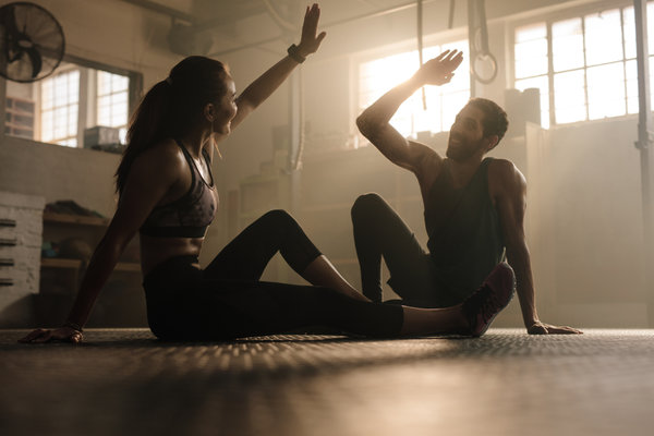 man and woman sat on floor giving each other a high five as they discuss three exercise tips backed by science