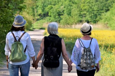 three women wth their backs to the camera going through the perimenopause together. They are holdng hands in support.