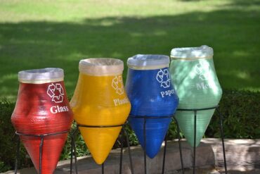 4 different coloured ecycling bins in a park