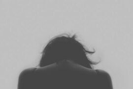 Black and white photo of thee back of a woman from the shoukders up, bowing her head as she has a chronic pain condition