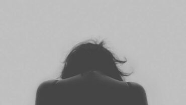 Black and white photo of thee back of a woman from the shoukders up, bowing her head as she has a chronic pain condition