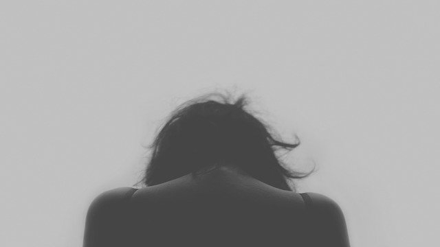 Black and white photo of thee back of a woman from the shoukders up, bowing her head as she has a chronic pain condition