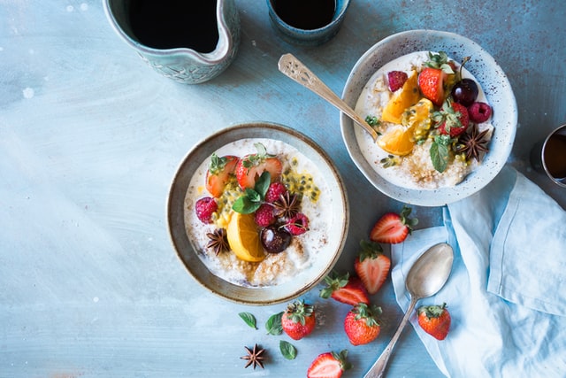 two bowls of oatmeal on a table with strawberries and a spoon scattered around