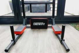 close up picture of the onetwofit wallmounted pull up bar. it is sat on a wooden floor in fron of some glass bi fold doors looking out onto a patio area