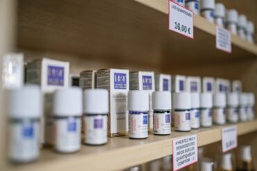 Rows of small remedy bottles with price tags on wooden shop shelves