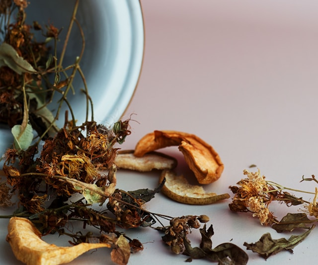 Dried herbs, flowers, and botanical pieces spilling from a bowl onto a pale surface