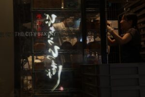 A shopper reaching into a glass door chiller cabinet in a small food shop